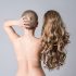 Topless woman with curly blonde wig on gray studio background, naked female back